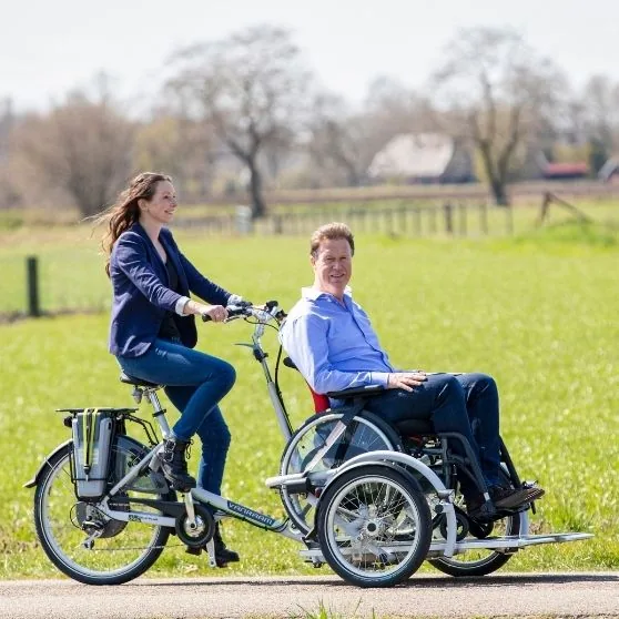 Pair using a wheelchair transport bike with the wheelchair user seated in the front of the bike.