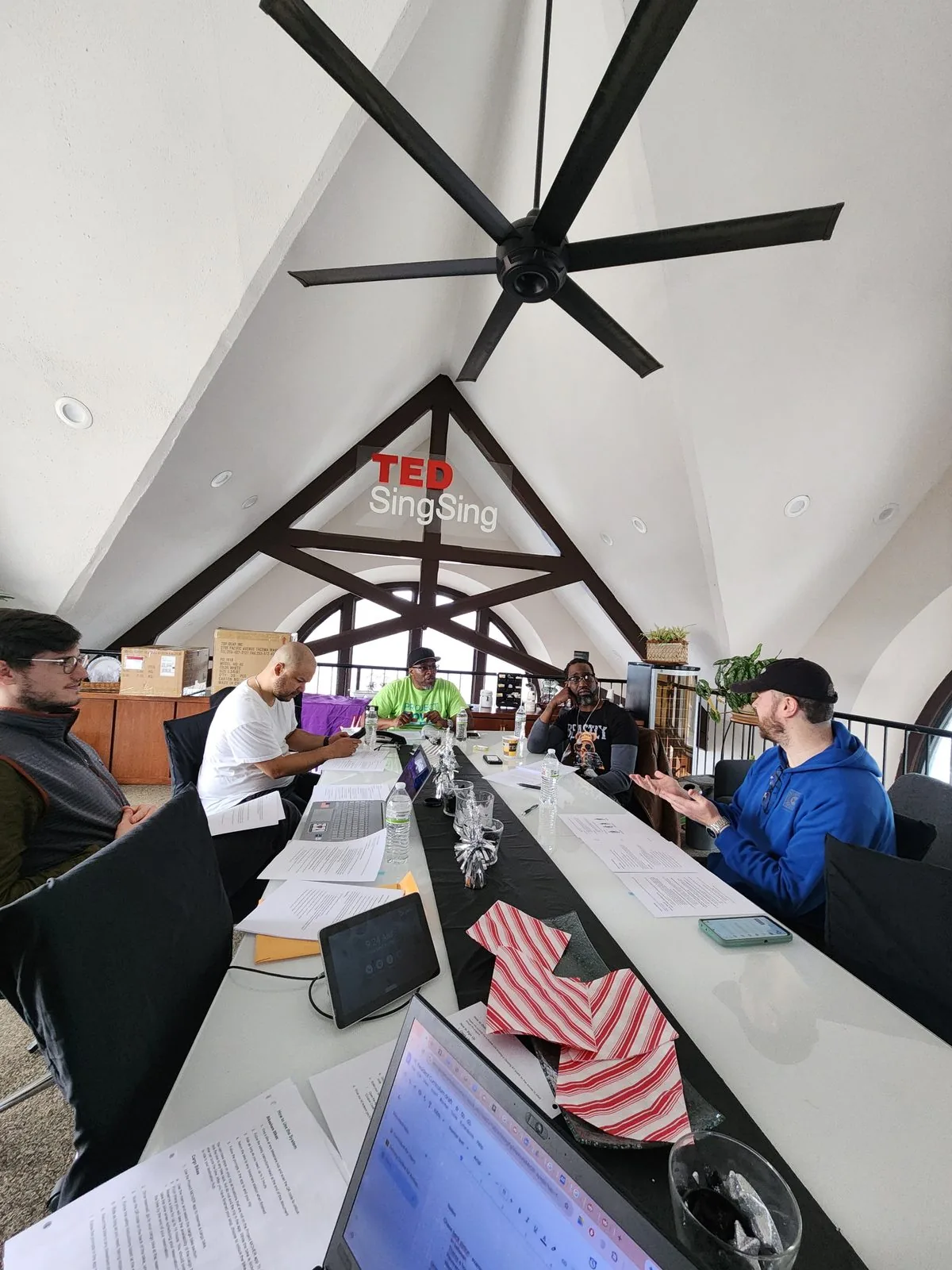 A working session around a long table under a vaulted timber ceiling, participants with laptops, printed agendas and notes in front of them