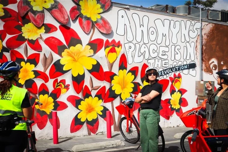 E-bike riders stop during group ride in front of mural in Pacoima, Los Angeles
