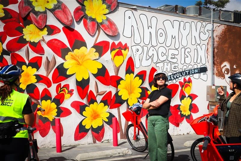 E-bike riders stop during group ride in front of mural in Pacoima, Los Angeles