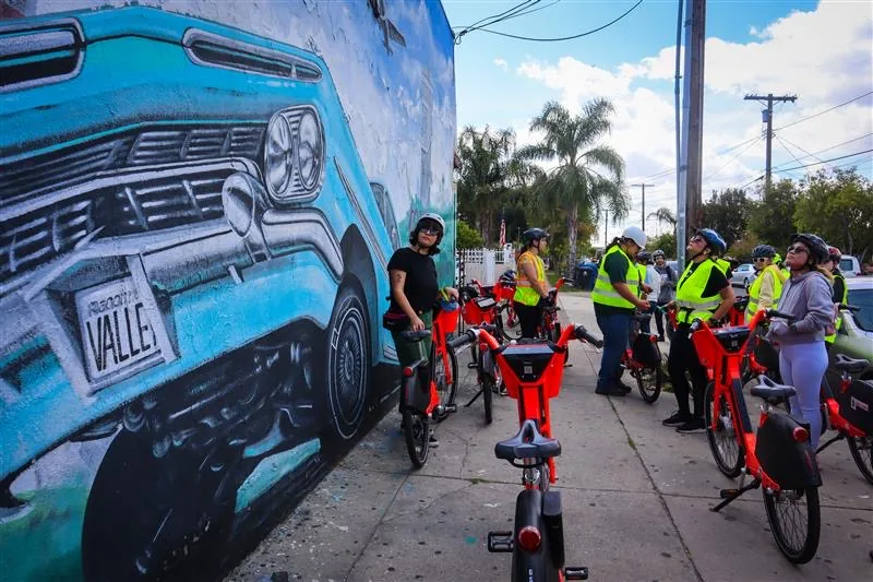 E-bike riders stopped in front of a mural during a group bike ride in Pacoima, Los Angeles