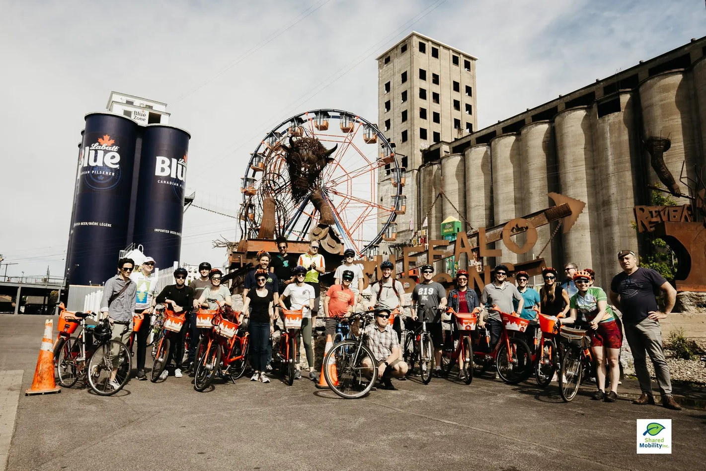 A large group of cyclists lined up with their bicycles in front of Buffalo's grain silos