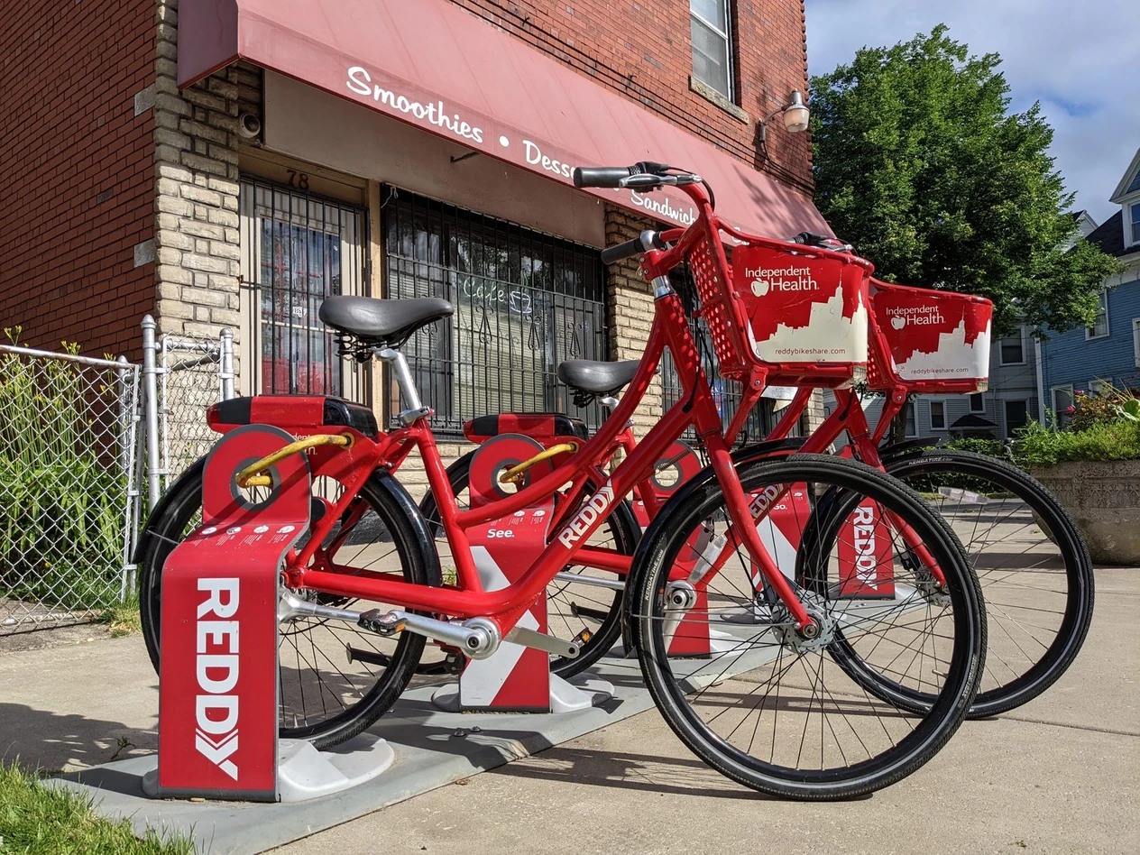 Red Reddy bikes docked at a station outside a corner smoothie shop