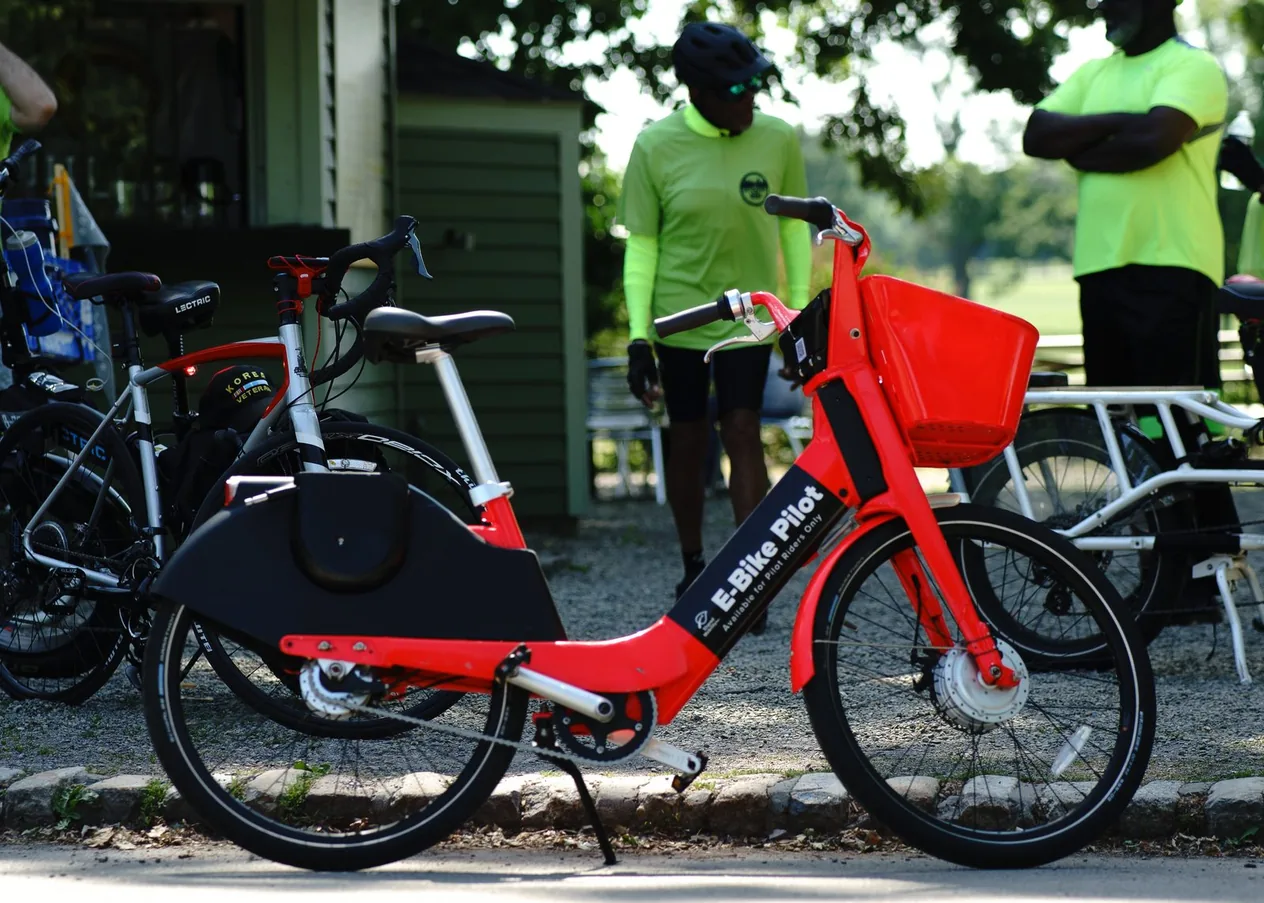 A red e-bike marked E-Bike Pilot, with people in bright green shirts behind it