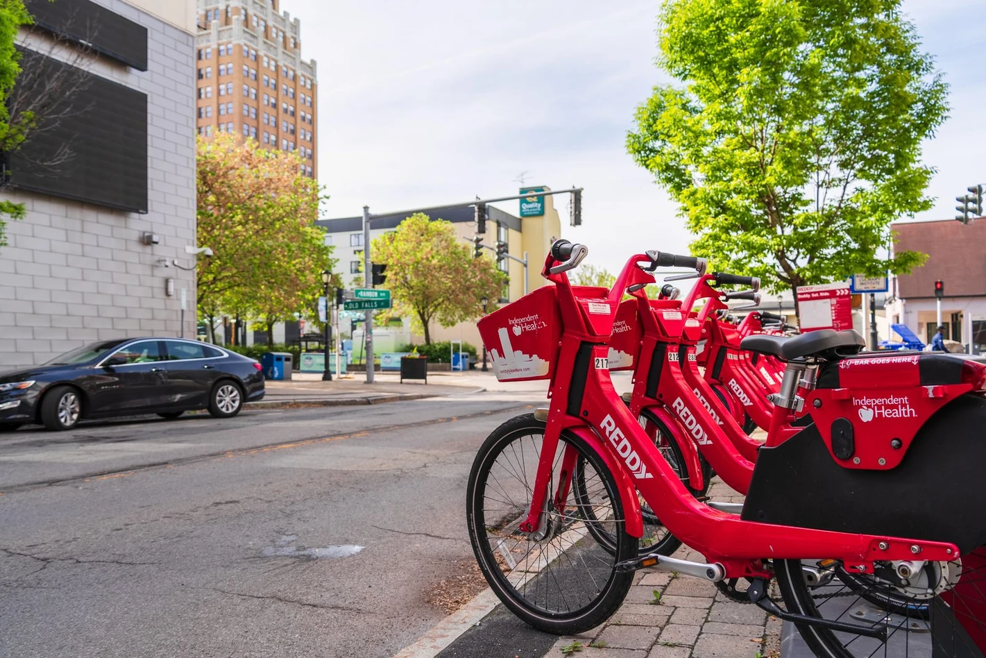 A row of red Reddy bikes docked at a station on a Buffalo street corner