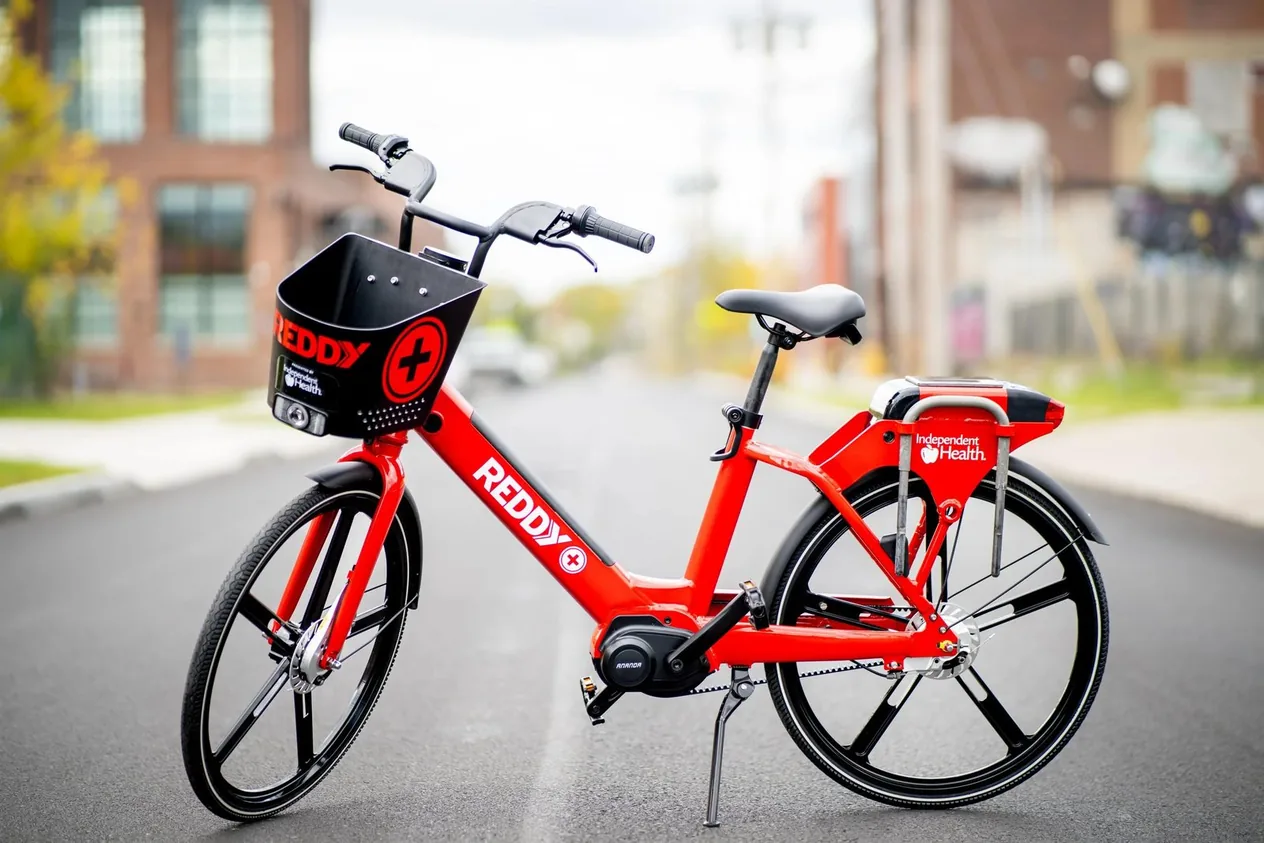 A red Reddy+ pedal-assist e-bike parked on a city street