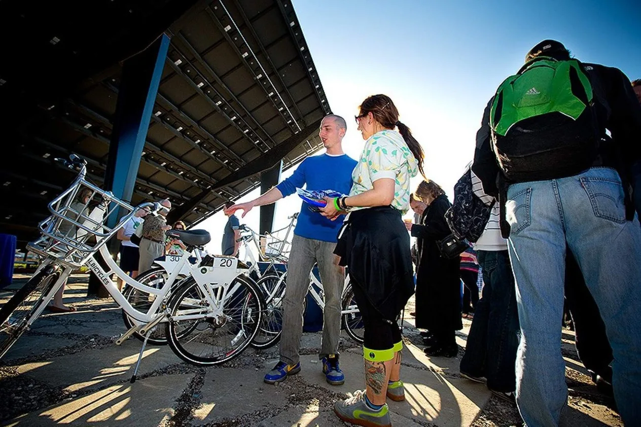 People gathered around white bikeshare bikes under a canopy at the 2012 campus pilot